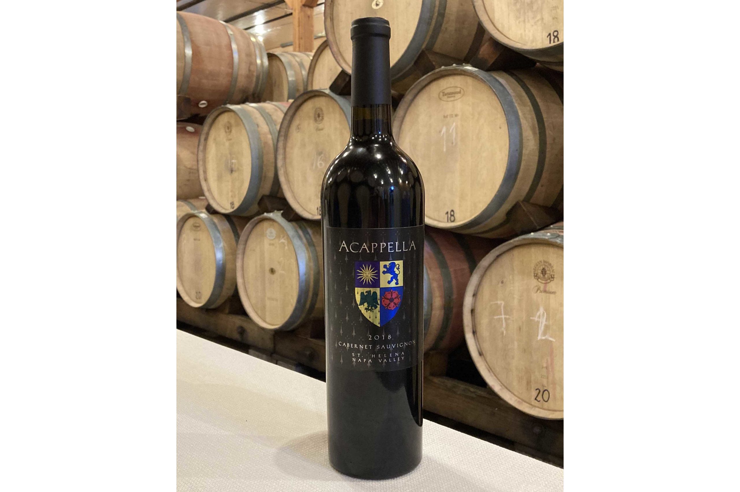 A bottle of the 2018 Acappella Cabernet Sauvignon in front of barrels in the winery