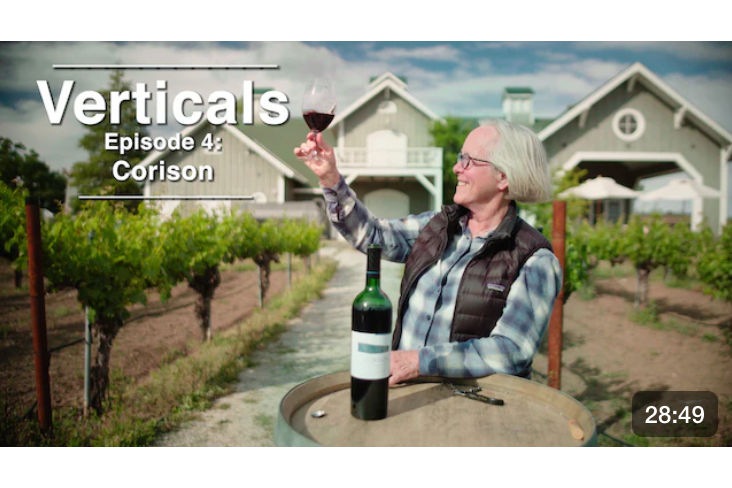 SommTV Screenshot of their Corison Episode titled "Verticals" - photo of Cathy Corison with a glass of her Corison Cabernet and the Corison Winery in the background.