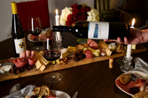 Winter Holiday table with person pouring a bottle of Corison Cabernet Sauvignon with candles, cheese, crackers and holiday decorations