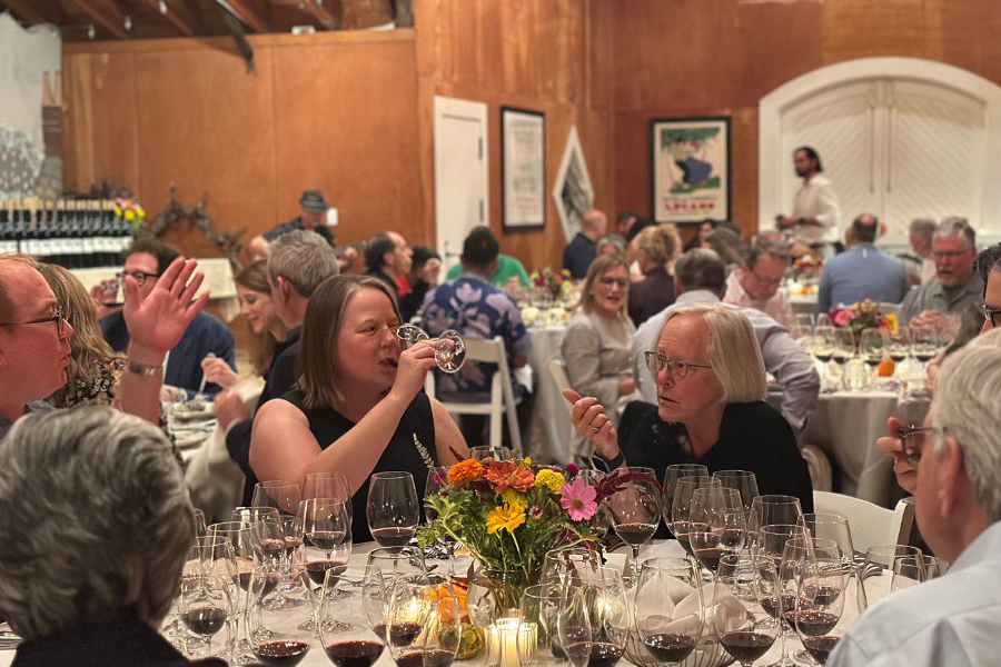 Cathy Corison and wine club guests at a table upstairs in the winery, talking, tasting wine and eating dinner.