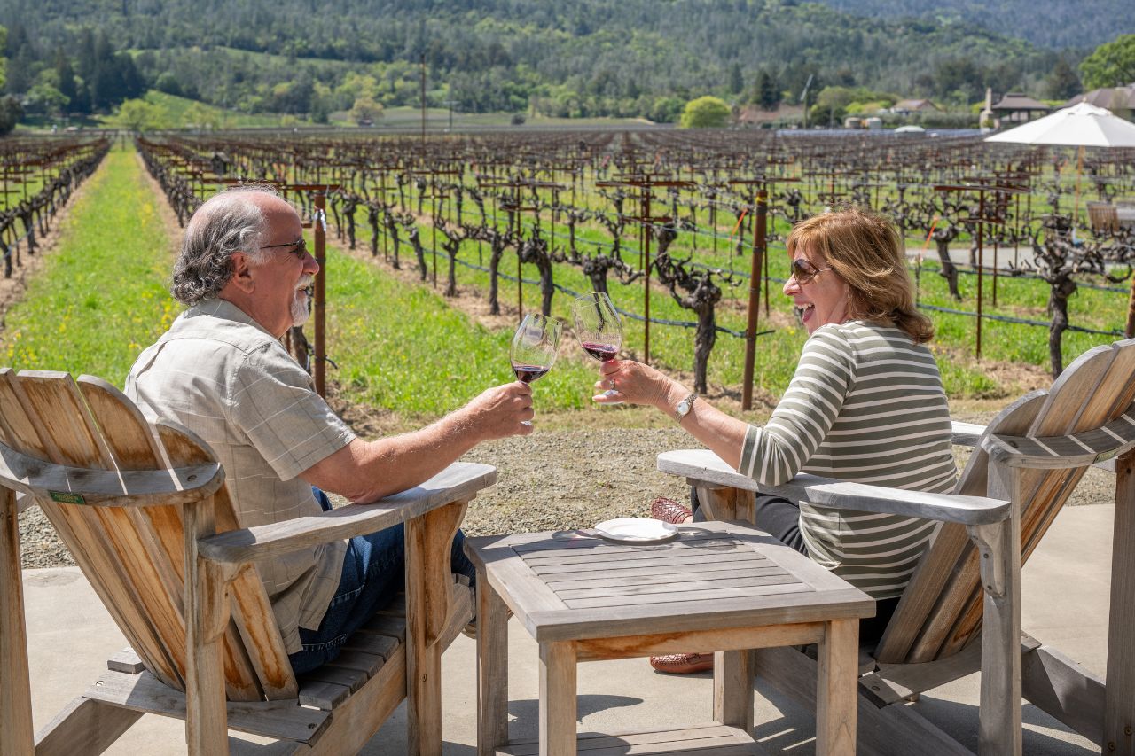 Two club members lounging by Kronos Vineyard at last year's spring party, toasting with Kronos Vineyard Cabernet Sauvignon.