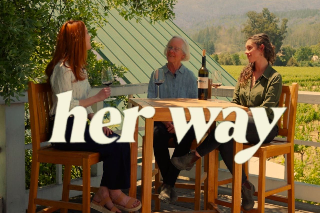 Kelsey Glasser, Cathy Corison and Grace Corison Martin talking out on the balcony at the winery overlooking Kronos Vineyard. The "Her Way" logo is over the photo.